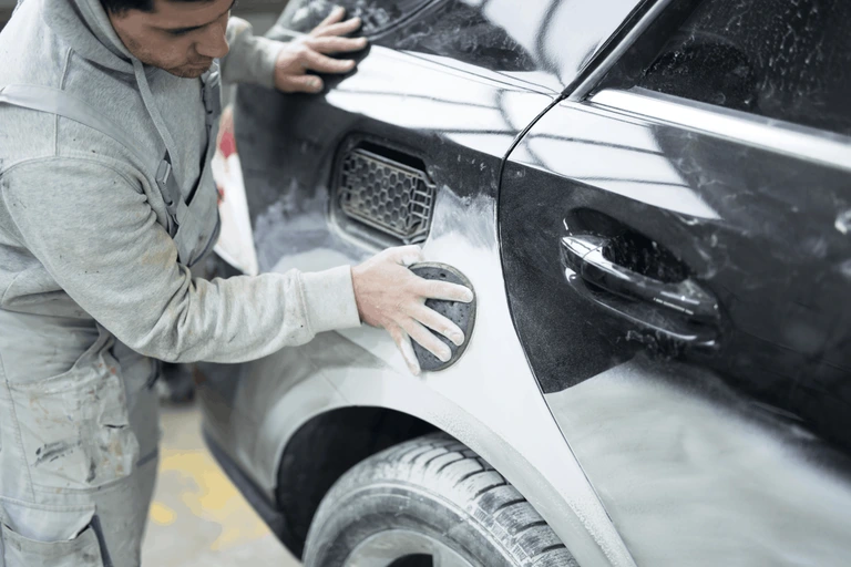 man sanding a car at an auto body shop
